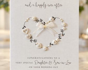 May include: A white textured wedding greeting card featuring a heart-shaped wreath of black printed vines, white pearls, and heart-shaped beads. A sheer white ribbon bow sits at the top center. Text reads: WISHING YOU BOTH LOVE, LAUGHTER and a happily ever after CONGRATULATIONS TO A VERY SPECIAL Daughter & Son-in-Law ON YOUR WEDDING DAY Olivia Mai & Oliver James.