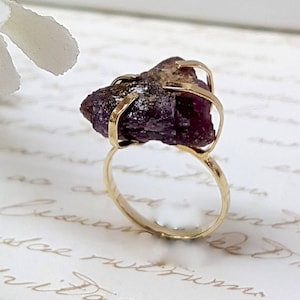 May include: A gold ring with a large, raw, purple amethyst stone set in the center. The stone is held in place by gold wire.