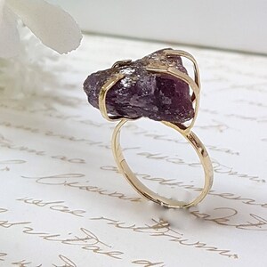May include: A gold ring with a large, purple amethyst gemstone set in a wire cage design.