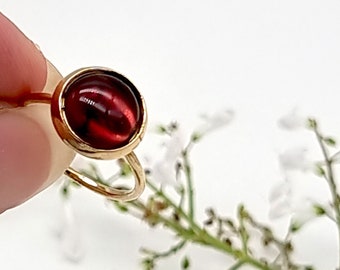 May include: A gold ring with a deep red cabochon gemstone.