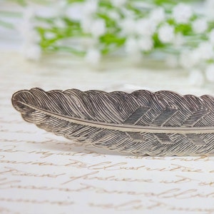 May include: A silver feather bookmark with a detailed design. The feather is curved and has a pointed tip.