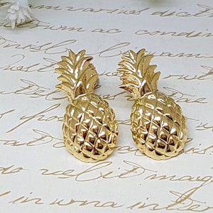 Op de afbeelding: Een paar gouden ananas oorbellen. De oorbellen zijn gemaakt van metaal en hebben een gedetailleerd ananas ontwerp.