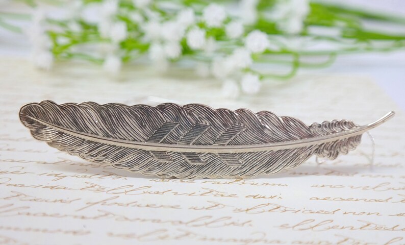 May include: A silver feather bookmark with a detailed design. The feather is curved and has a pointed tip.