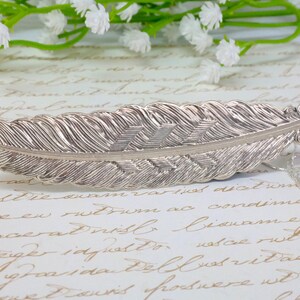 May include: A silver feather pendant necklace with a delicate chain and a small charm. The feather is detailed with a textured design.
