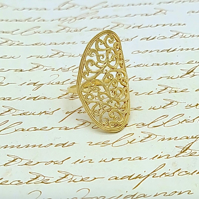 May include: A gold filigree ring with a delicate, intricate design. The ring is oval shaped and has a wide band.
