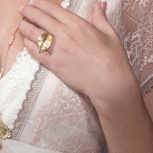 Puede incluir: Un anillo de hoja de oro con un dise&ntilde;o detallado. El anillo se lleva en el dedo &iacute;ndice de una mano.