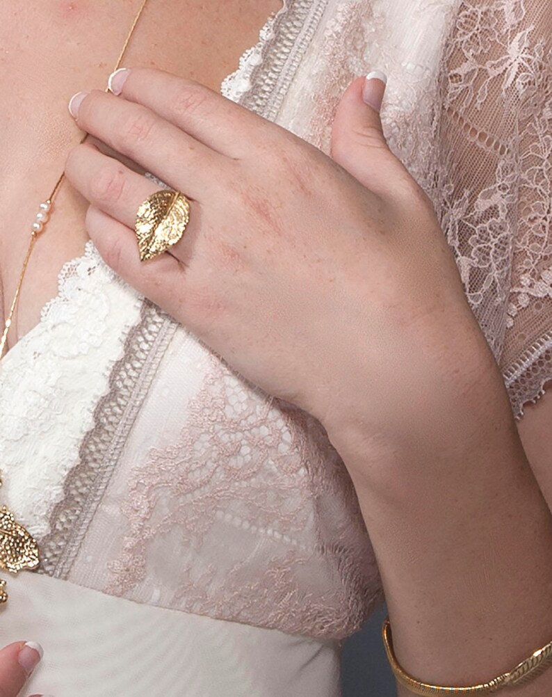 Puede incluir: Un anillo de hoja de oro con un dise&ntilde;o detallado. El anillo se lleva en el dedo &iacute;ndice de una mano.