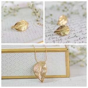 Puede incluir: Un collar con un colgante de hoja de oro y un anillo de hoja de oro. El collar est&aacute; sobre una caja blanca con un borde dorado. El anillo est&aacute; sobre una superficie blanca con un patr&oacute;n floral.