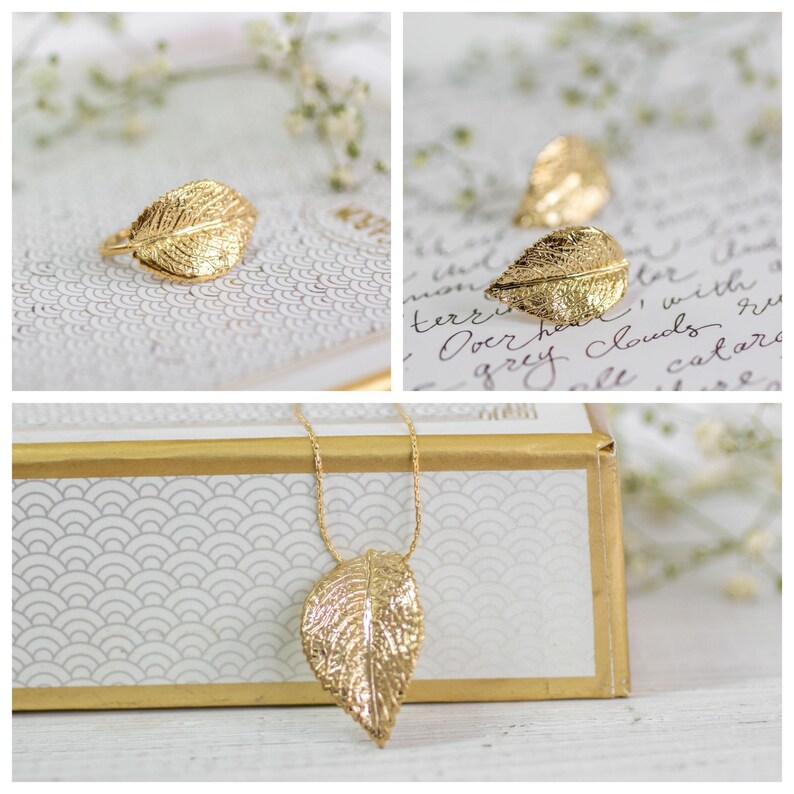 Puede incluir: Un collar con un colgante de hoja de oro y un anillo de hoja de oro. El collar est&aacute; sobre una caja blanca con un borde dorado. El anillo est&aacute; sobre una superficie blanca con un patr&oacute;n floral.
