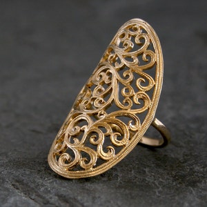 May include: A gold filigree ring with a delicate, intricate design. The ring is open and has a wide band.