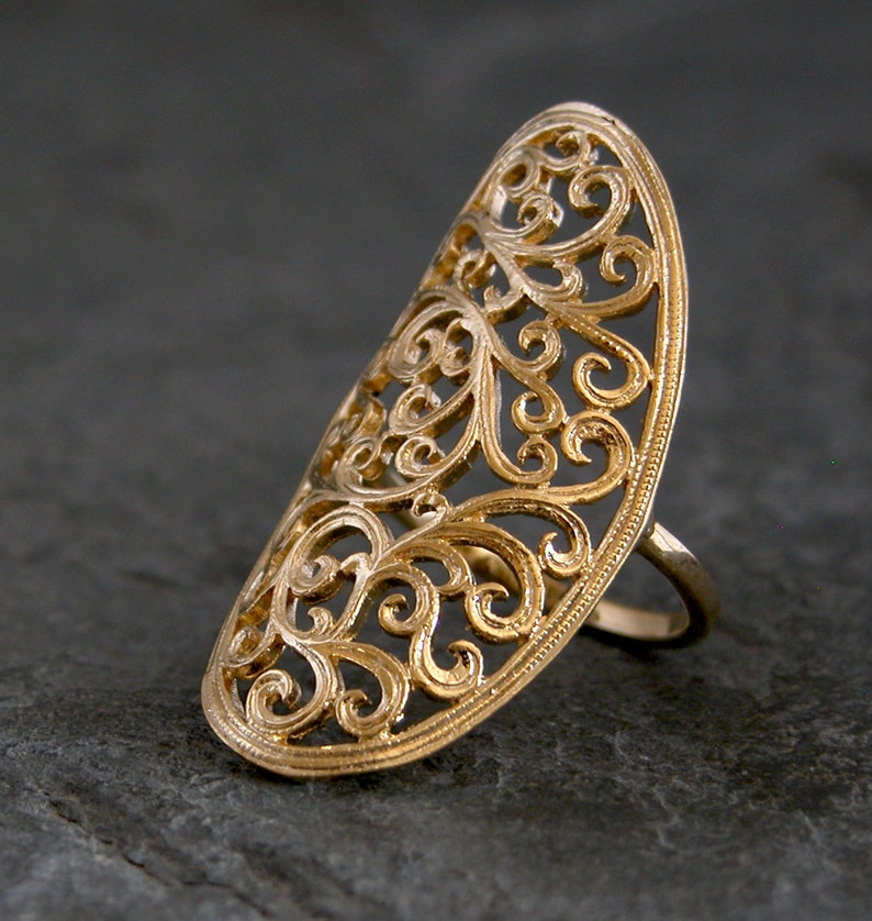 May include: A gold filigree ring with a delicate, intricate design. The ring is open and has a wide band.