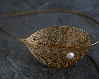 May include: Gold leaf headband with a delicate pearl accent. The leaf design is intricate and detailed, making it a beautiful and unique accessory.