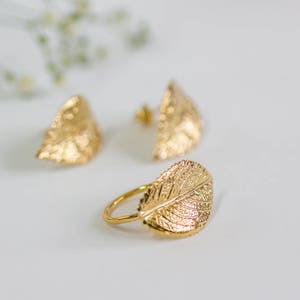 Puede incluir: Un conjunto de pendientes y un anillo de hoja de oro. Los pendientes tienen forma de hoja y una superficie texturizada. El anillo tambi&eacute;n tiene forma de hoja y una superficie texturizada.