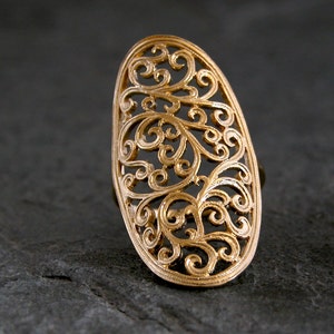 May include: A gold filigree ring with a delicate, intricate design. The ring is oval shaped and has a large, open centre.