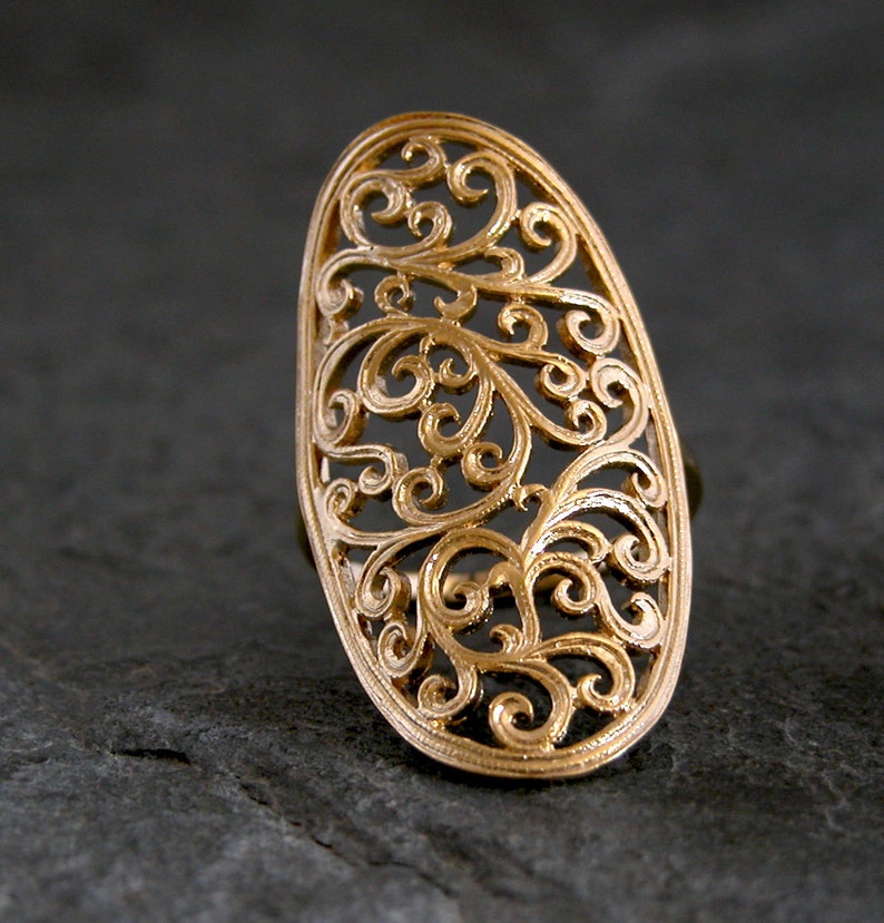May include: A gold filigree ring with a delicate, intricate design. The ring is oval shaped and has a large, open centre.