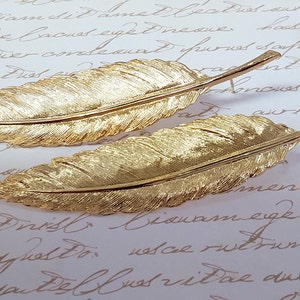 May include: A pair of gold feather earrings. The earrings are long and dangle, with a feather design. The feathers are detailed and realistic.