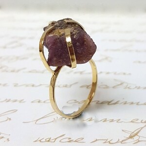 May include: A gold ring with a large, raw pink gemstone set in a cage-like design.