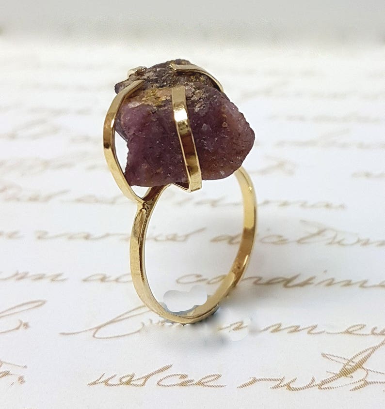 May include: A gold ring with a large, raw pink gemstone set in a cage-like design.