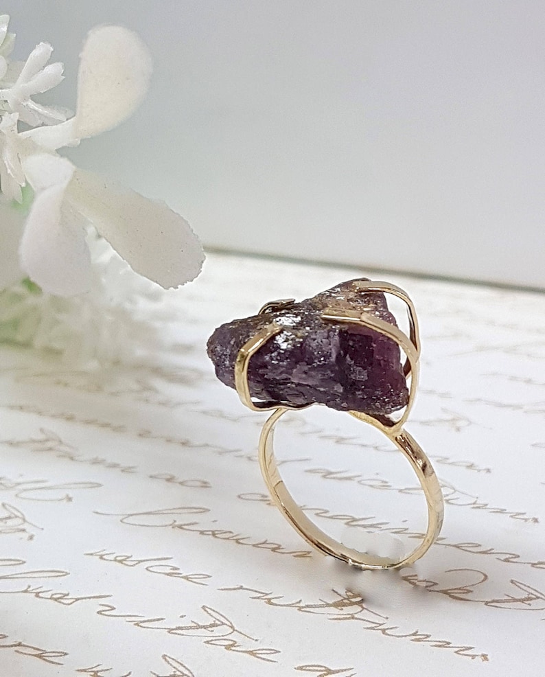 May include: A gold ring with a large, purple amethyst gemstone set in a wire cage design.