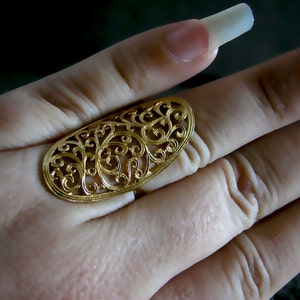 May include: A gold filigree ring with a delicate, intricate design. The ring is oval shaped and has a cutout pattern of swirling leaves and flowers.