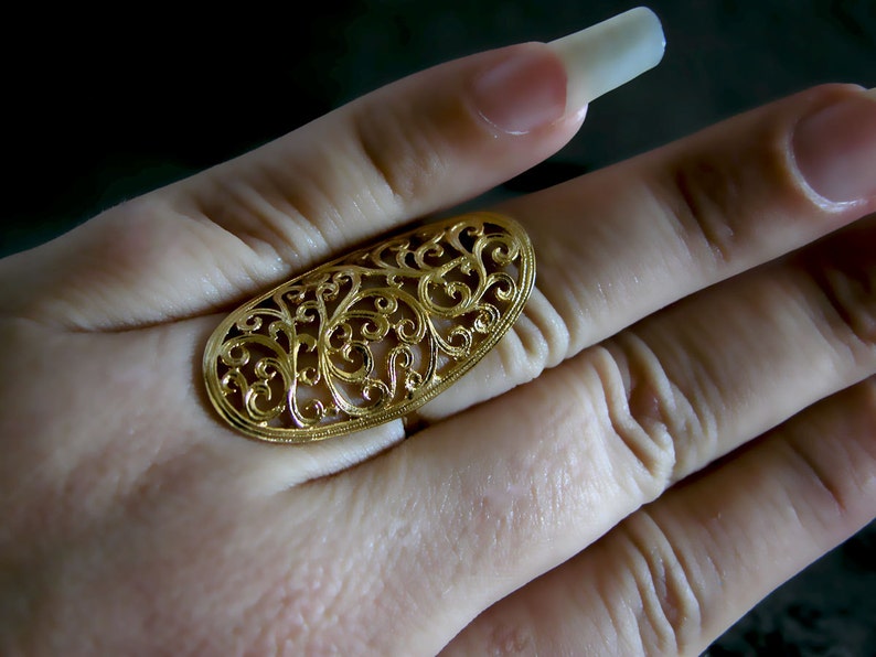 May include: A gold filigree ring with a delicate, intricate design. The ring is oval shaped and has a cutout pattern of swirling leaves and flowers.