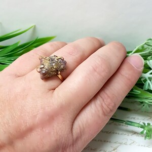 May include: A gold ring with a pink and gold crystal stone. The ring is on a hand.