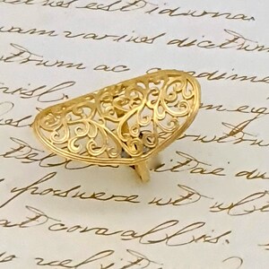 May include: A gold filigree ring with a delicate, intricate design. The ring is shaped like a half-circle and has a floral pattern.