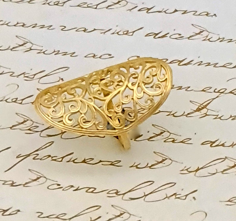 May include: A gold filigree ring with a delicate, intricate design. The ring is shaped like a half-circle and has a floral pattern.