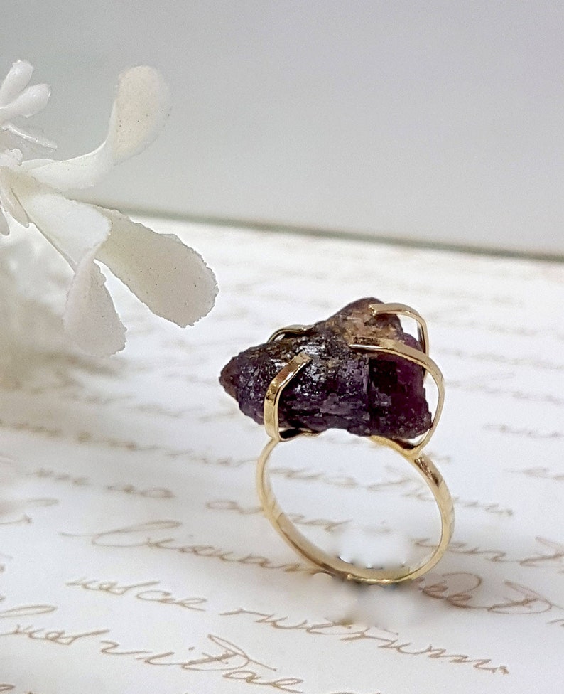 May include: A gold ring with a large, raw, purple amethyst stone set in the center. The stone is held in place by gold wire.