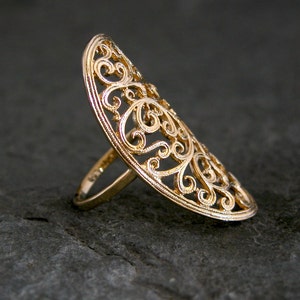 May include: A gold filigree ring with a delicate, intricate design. The ring is open and has a wide band.