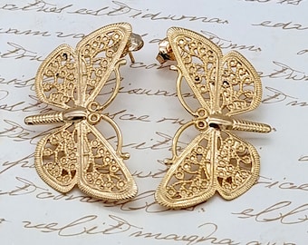 May include: A pair of gold butterfly earrings with intricate filigree designs. The earrings are made of metal and have a delicate, feminine look.