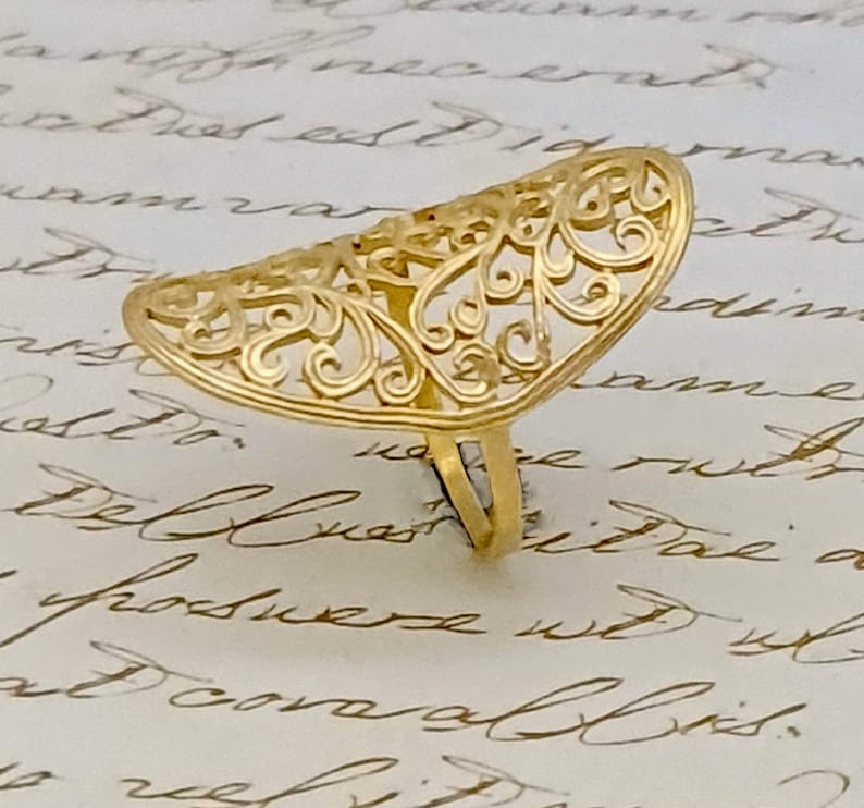 May include: A gold filigree ring with a delicate, intricate design. The ring is open and has a curved shape.
