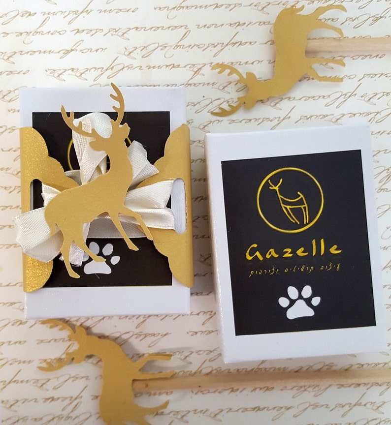 May include: Two white boxes with black and gold accents. One box has a gold deer cutout and a white ribbon. The other box has the word "Gazelle" in gold, a deer logo, and a paw print. Decorative gold deer cutouts are scattered around.