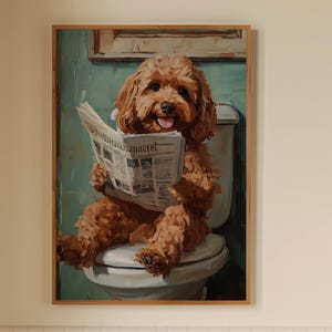Puede incluir: Una obra de arte enmarcada representa a un perro marrón sentado en un inodoro, leyendo un periódico. El perro tiene un pelaje esponjoso y está sonriendo. La obra de arte se exhibe en un baño con un pequeño taburete de madera, una toalla y una botella de jabón.