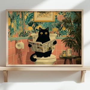 Könnte beinhalten: Gerahmter Kunstdruck, der eine schwarze Katze auf einer Toilette zeigt, die eine Zeitung liest. Die Zeitung trägt das Wort "Paws". Das Badezimmer hat rosa Fliesen, florale Tapeten und einen kleinen Beistelltisch.