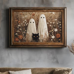 May include: A framed artwork depicts two white ghost figures in a field of flowers, with a black cat peeking out from the foliage. The artwork is in a wooden frame, and the color palette is muted with earthy tones.