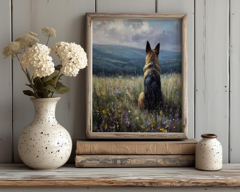 May include: A framed print of a German Shepherd dog sitting in a field of wildflowers, facing away from the viewer. The artwork is displayed on a wooden shelf with a white vase of flowers and a small speckled jar.