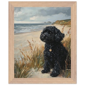 Könnte beinhalten: Gerahmtes Gemälde eines schwarzen Hundes, der an einem Sandstrand sitzt und aufs Meer blickt. Das Kunstwerk zeigt eine Küstenlandschaft mit bewölktem Himmel und grasbewachsenen Dünen in einem hellen Holzrahmen.
