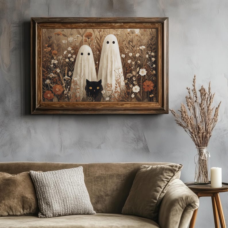 May include: A framed artwork depicts two white ghost figures in a field of flowers, with a black cat peeking out from the foliage. The artwork is in a wooden frame, and the color palette is muted with earthy tones.