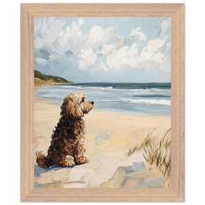 May include: Framed art print of a dog sitting on a beach, gazing at the ocean. The artwork features a light brown dog with a fluffy coat, set against a backdrop of a sandy beach, blue water, and a cloudy sky. The frame is light brown.
