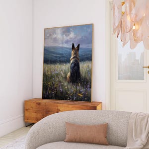 May include: A framed artwork depicts a German Shepherd dog sitting in a field of wildflowers, facing away from the viewer. The painting has a gold frame and is displayed on a wooden cabinet. The scene is set against a backdrop of rolling hills and a cloudy sky.