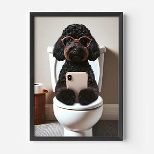 Puede incluir: Impresión enmarcada de un caniche negro con gafas naranjas y sosteniendo un teléfono inteligente mientras está sentado en un inodoro. Un rollo de papel higiénico está sobre una pequeña mesa auxiliar tejida. El tema es humorístico.