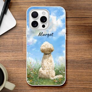 May include: A phone case with a dog illustration. The design depicts a cream-coloured dog sitting in a field of wildflowers under a blue sky with clouds. The name "Margot" is written in script above the dog.