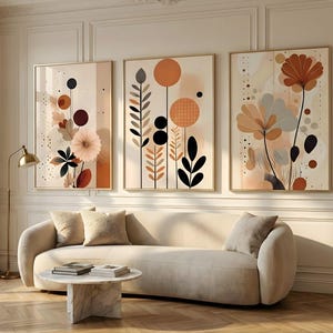 Könnte beinhalten: Ein Set aus drei gerahmten Wandkunstdrucken mit abstrakten botanischen Illustrationen in Terrakotta, Beige, Schwarz und Creme. Die Kunstwerke zeigen stilisierte Blumen, Blätter und geometrische Formen in einer vertikalen Anordnung.