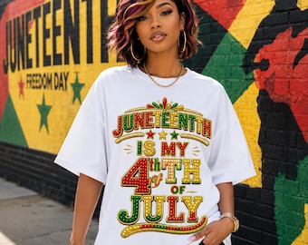 May include: A white short-sleeved t-shirt featuring a graphic print with the text JUNETEENTH IS MY 4th OF JULY in red, green, and yellow lettering with a dotted pattern. The design includes small star icons and decorative curved lines in the same colors.