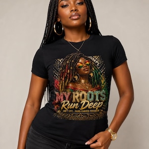 Op de afbeelding: Zwart T-shirt met de tekst "MY ROOTS RUN DEEP" en een illustratie van een vrouw met kleurrijke dreadlocks en een zonnebril. Het shirt heeft ook de tekst "SOFT LIFE...HARD-EARNED FREEDOM". De vrouw draagt gouden sieraden.