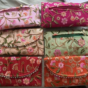 May include: A collection of six embroidered clutch purses in various colors, including pink, red, orange, and green. Each purse features floral embroidery, sequins, and a beaded trim. The purses have a zippered top and a flap closure.