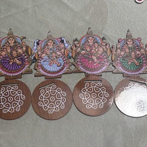 May include: A collection of eight wooden coasters and decorative figures. Each coaster is round with a white geometric design. The figures depict a deity with colorful details. The figures are connected to the coasters.