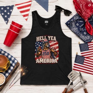 Pode incluir: Camiseta sem mangas preta com um gráfico que apresenta uma figura patriótica com o texto "HELL YEA 250 AMERICA". O design incorpora a bandeira americana e uma estética vintage. A camiseta sem mangas é cercada por decorações patrióticas.