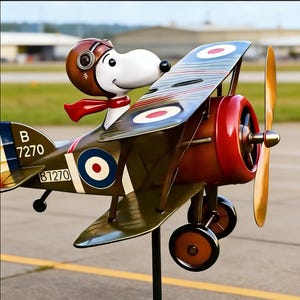 May include: A whimsical metal sculpture of Snoopy as a World War I flying ace in a biplane. The plane is painted in olive green, red, and brown with roundels. Snoopy wears a brown aviator helmet and a red scarf. The plane has the number B7270.